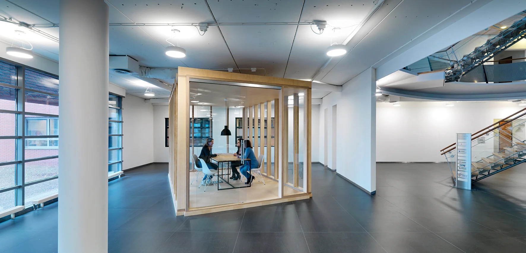 Modern kantoorinterieur met drie personen in vergadering in een glazen overlegruimte aan de Pompmolenlaan.