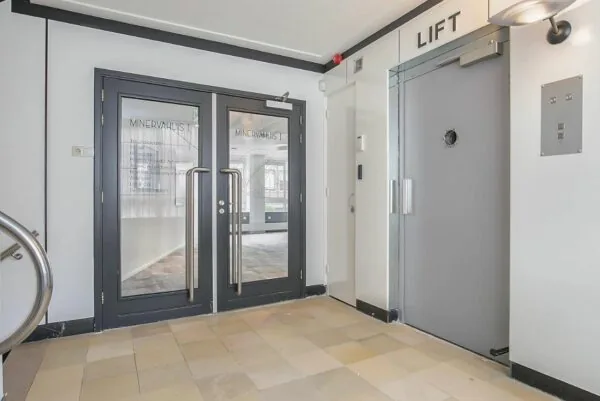 Hal met dubbele glazen deuren naar Minervahuis I en een grijze liftdeur rechts.