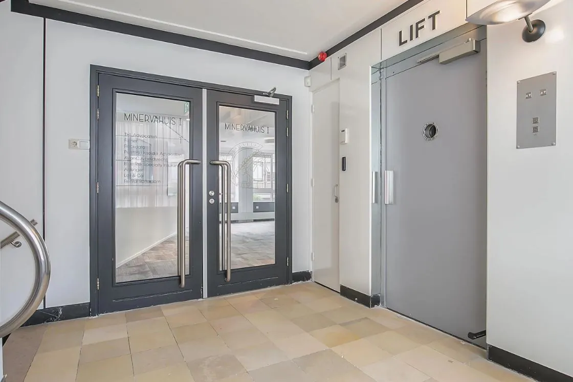 Hal met dubbele glazen deuren naar Minervahuis I en een grijze liftdeur rechts.