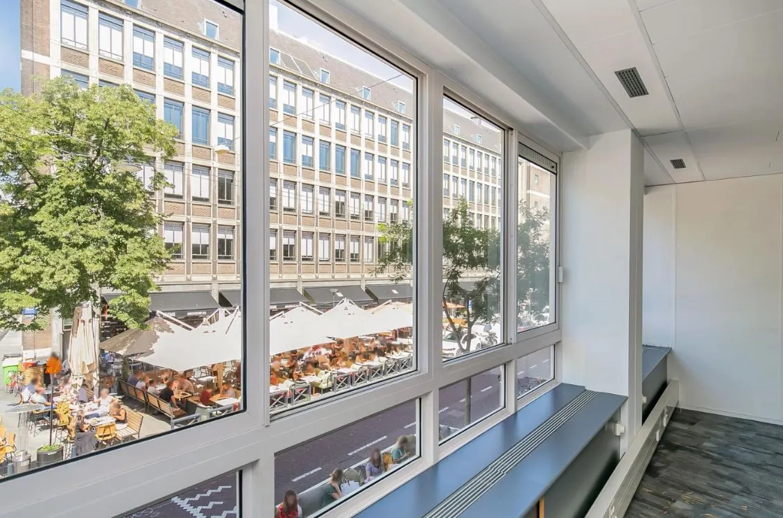 Uitzicht vanuit een modern kantoorpand op de Meent met terrassen en een groot kantoorgebouw aan de overkant.