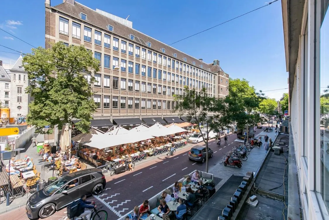 Drukke straat met terrassen en fietsers op de Meent in Rotterdam op een zonnige dag.