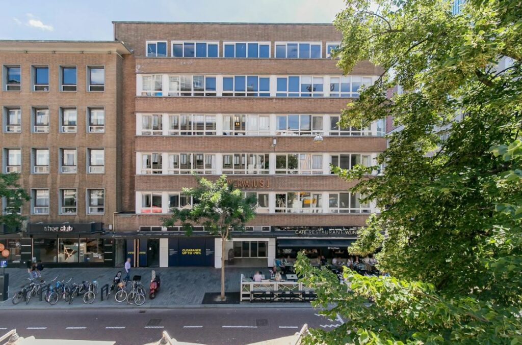 Voorgevel van het kantoorgebouw 'Nerfhuis 1' aan de Meent in Rotterdam met winkels, fietsenrekken en een terras op de begane grond.