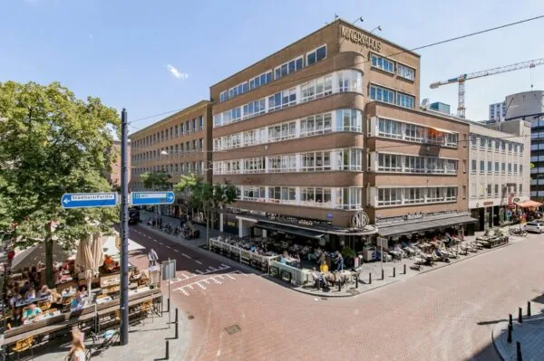 Straatbeeld met het Minervahuis in Rotterdam, waar mensen op terrassen zitten bij café-restaurant en wijnbar NRC.