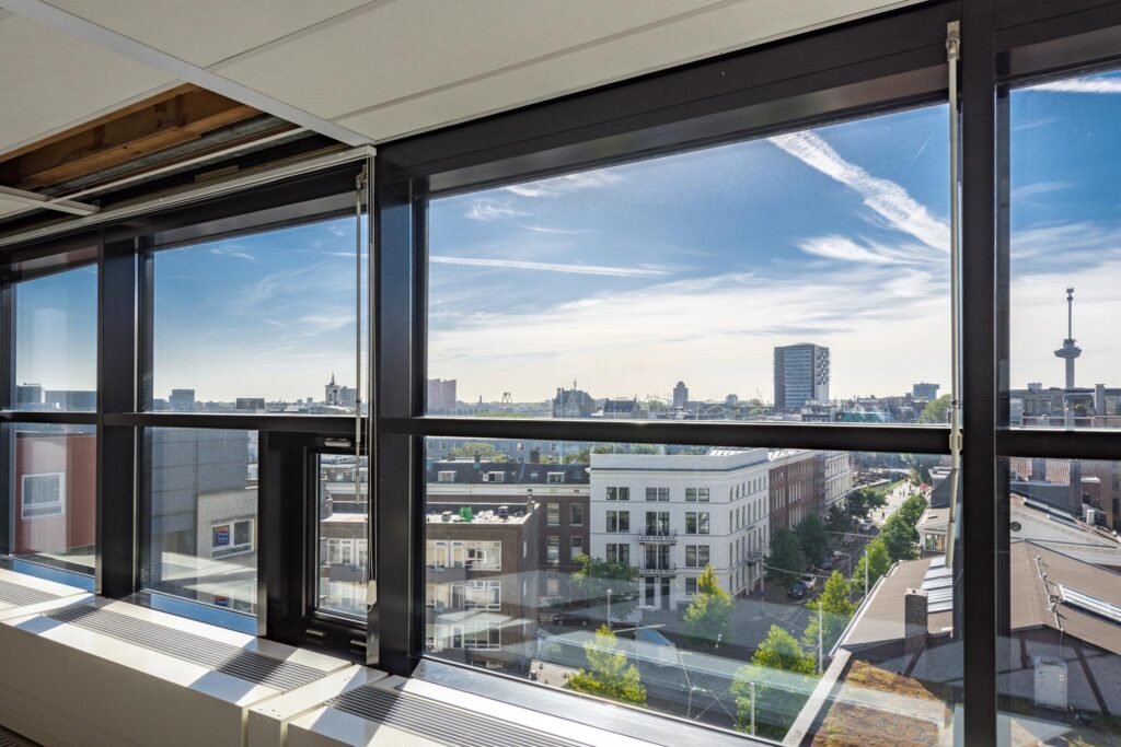 Uitzicht vanuit een hoog gebouw aan de Westerstraat op de skyline van Rotterdam met moderne en historische gebouwen.