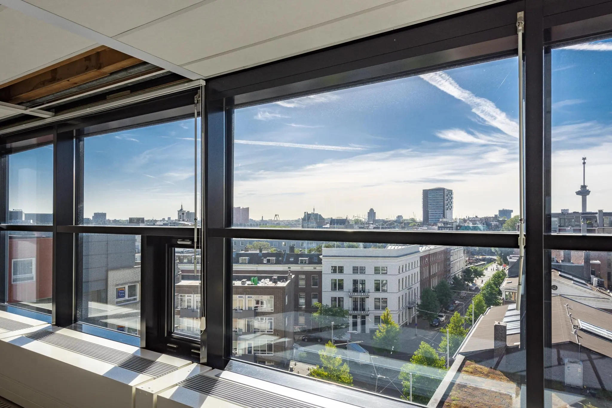 Uitzicht vanuit een hoog gebouw aan de Westerstraat op de skyline van Rotterdam met moderne en historische gebouwen.