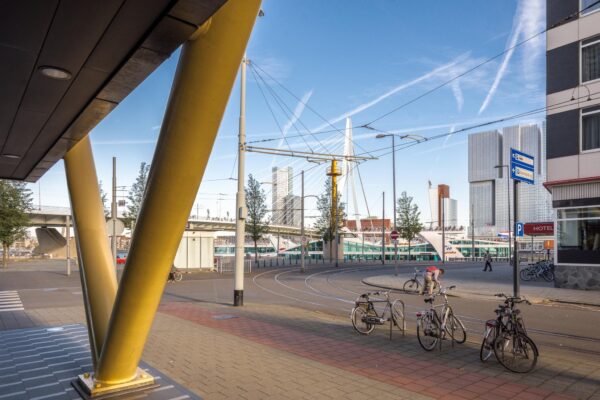 Straatbeeld van de Westerstraat in Rotterdam met zicht op de Erasmusbrug, fietspad, geparkeerde fietsen en moderne hoogbouw.