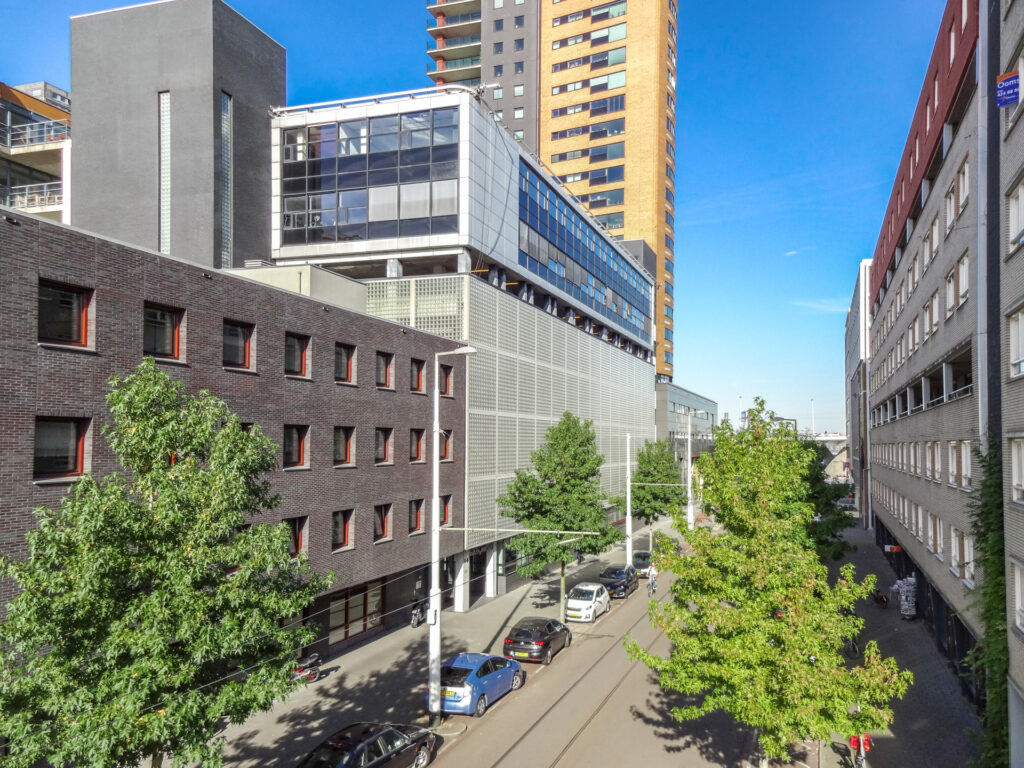 Zicht op de Westerstraat in een moderne stadsomgeving met hoge gebouwen, geparkeerde auto's en groene bomen.