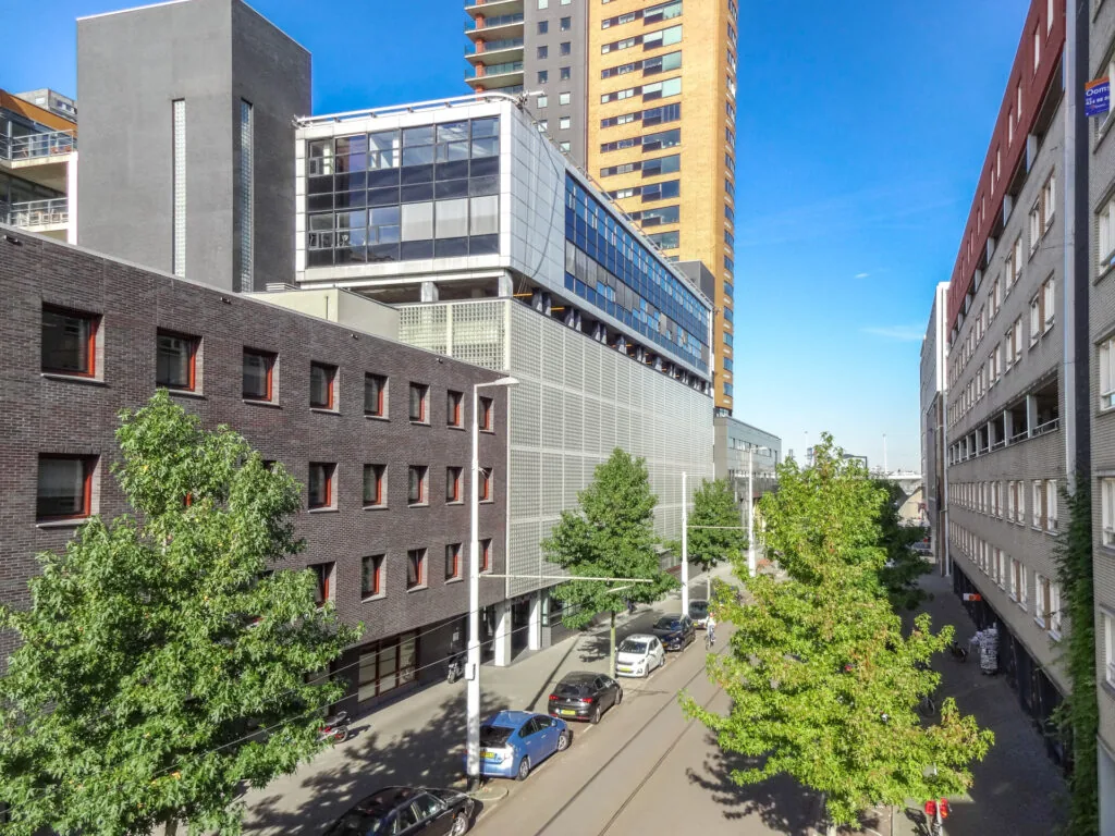 Zicht op de Westerstraat in een moderne stadsomgeving met hoge gebouwen, geparkeerde auto's en groene bomen.