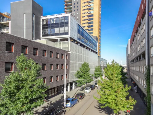Zicht op de Westerstraat in een moderne stadsomgeving met hoge gebouwen, geparkeerde auto's en groene bomen.