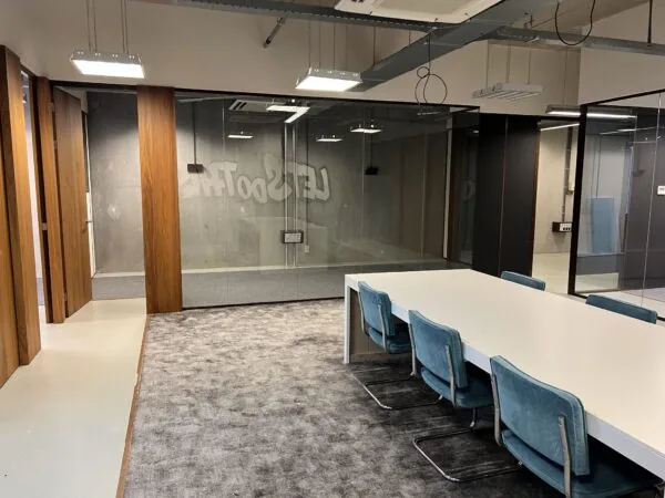 Moderne vergaderruimte aan de Danzigerkade met glazen wanden, een witte vergadertafel en blauwe stoelen.