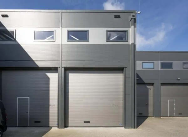 Grijze bedrijfspanden met grote overheaddeuren aan de Aalsmeerderweg onder een blauwe lucht.