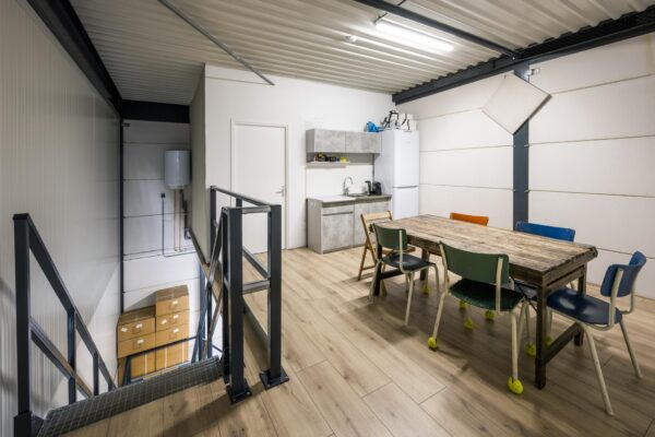 Bovenverdieping van een bedrijfsruimte aan de Aalsmeerderweg met een kantine met houten tafel, kleurige stoelen en kitchenette.