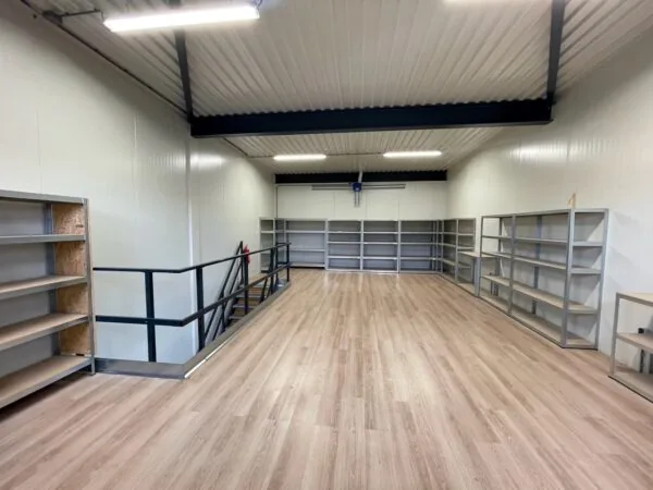 Magazijnruimte met houten vloer, metalen stellingen en trap aan de Aalsmeerderweg.