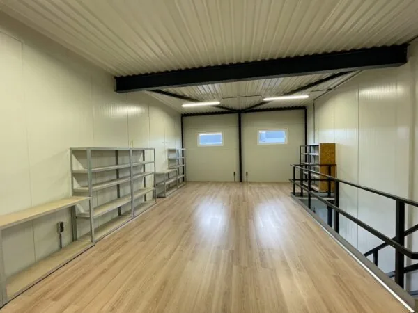 Op de verdieping van een loods aan de Aalsmeerderweg staan metalen stellingen langs de wand op een vloer met houtlook.