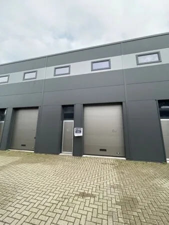 Grijze bedrijfspandunit aan de Aalsmeerderweg met te huur-bord naast de ingang.