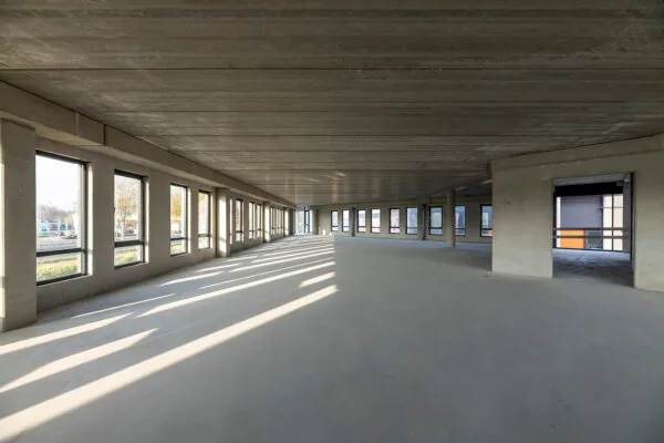 Leeg betonnen kantoorgebouw in aanbouw aan de Kringloopweg met grote ramen en binnenvallend zonlicht.