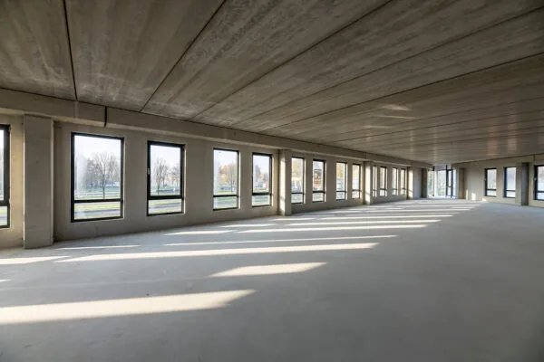 Leeg betonnen kantoorpand met grote ramen aan de Kringloopweg, waar zonlicht naar binnen valt.