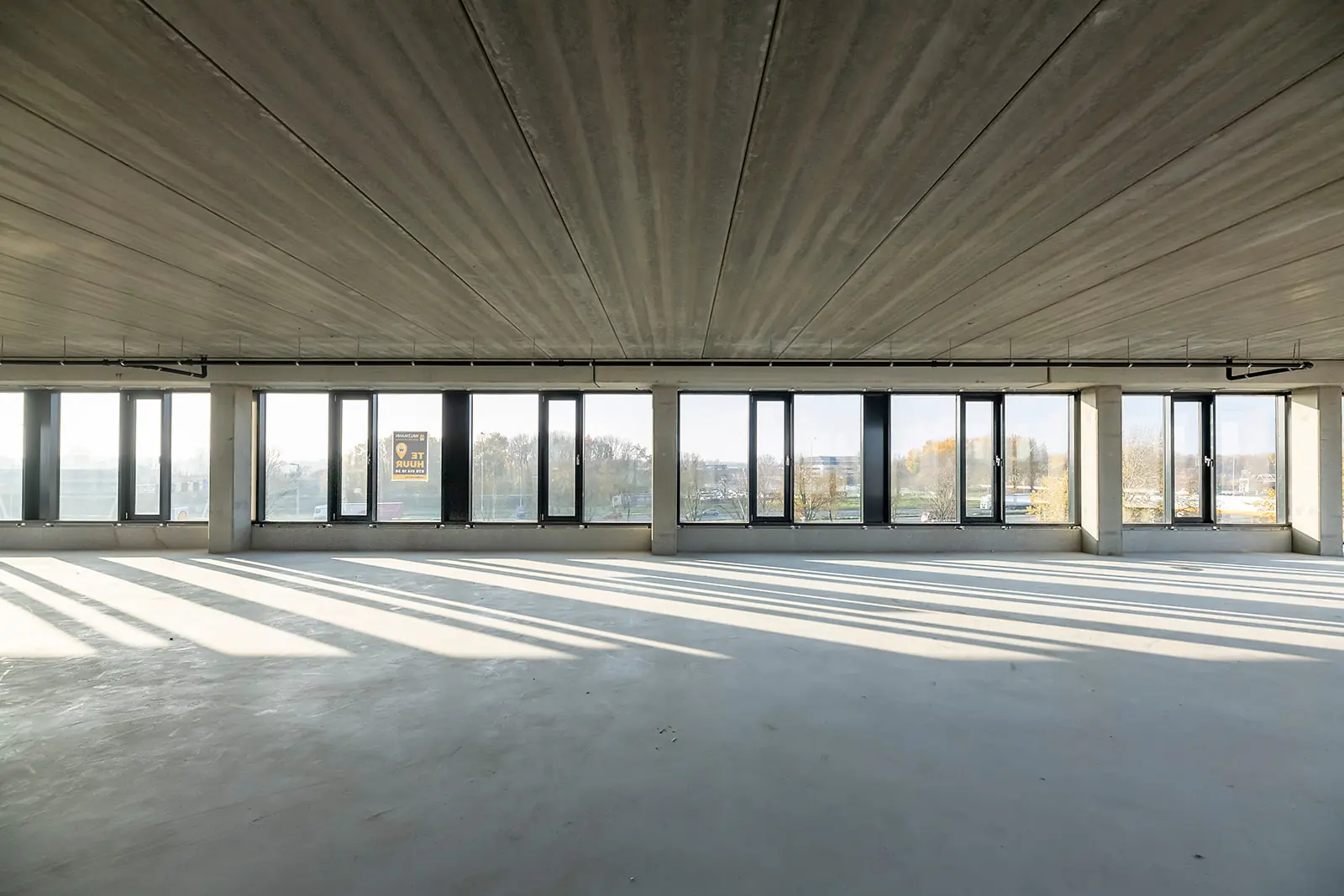 Leeg kantoorpand aan de Kringloopweg met grote ramen en betonvloer, met een "Te huur" bord zichtbaar.