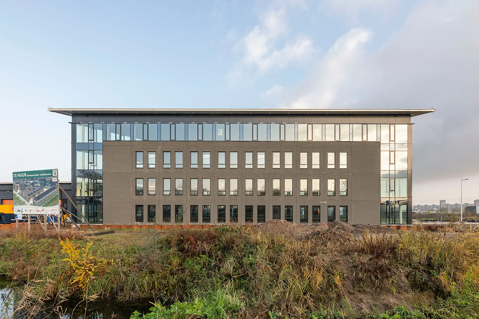Modern kantoorgebouw aan de Kringloopweg met te huur-bord op een braakliggend terrein.