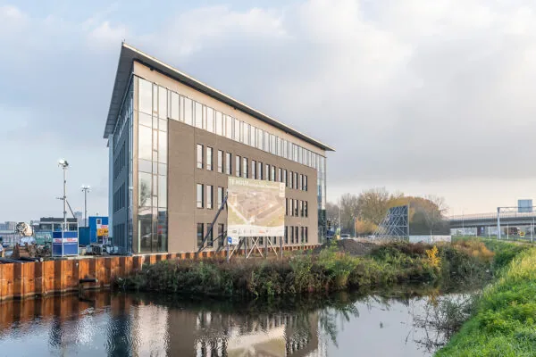 Kantoorgebouw aan de Kringloopweg met een "Te Huur"-bord aan het water bij een snelweg.