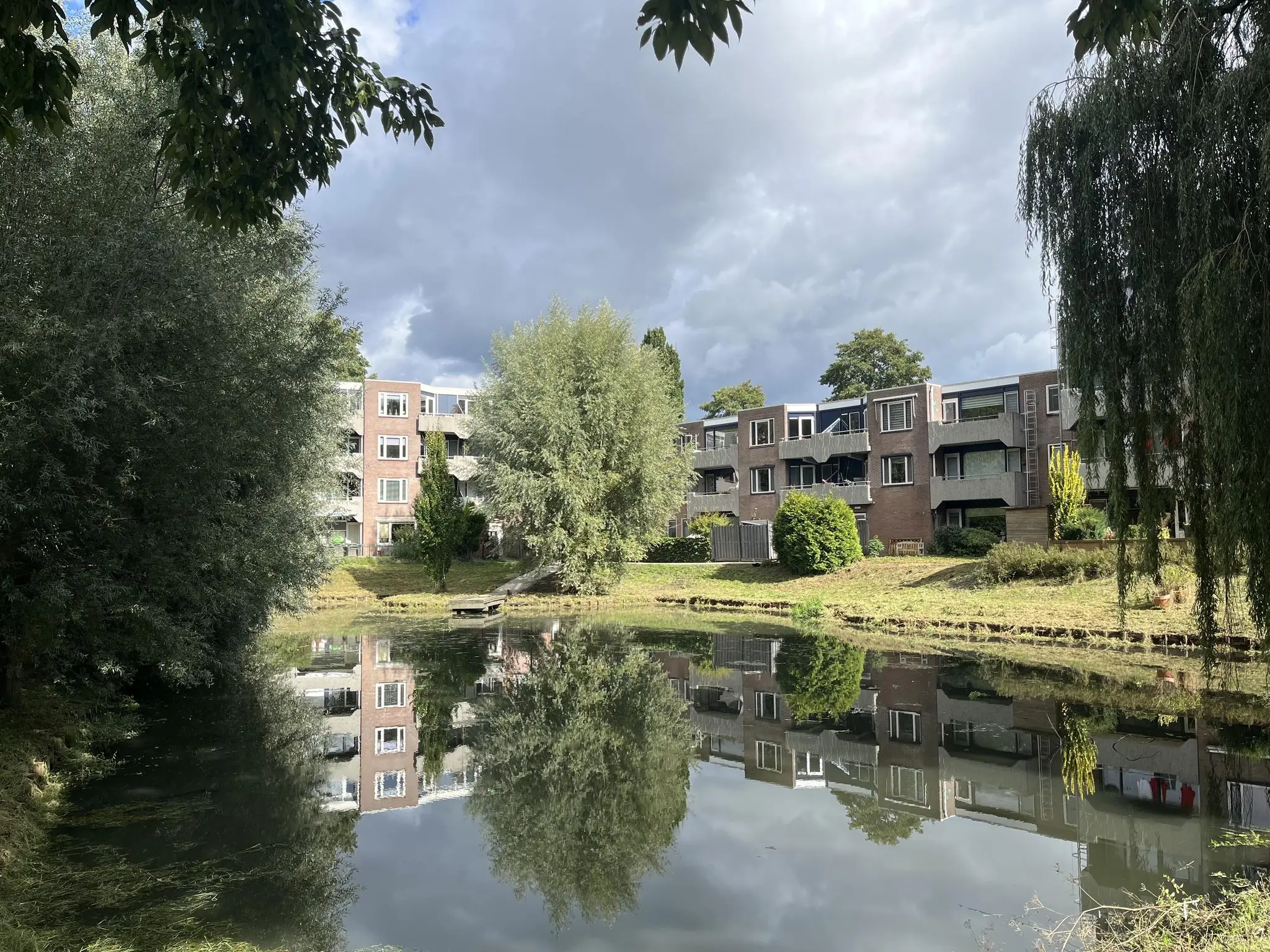 Appartementencomplex aan de Zoutkamperschans weerspiegeld in een rustige vijver, omgeven door bomen.
