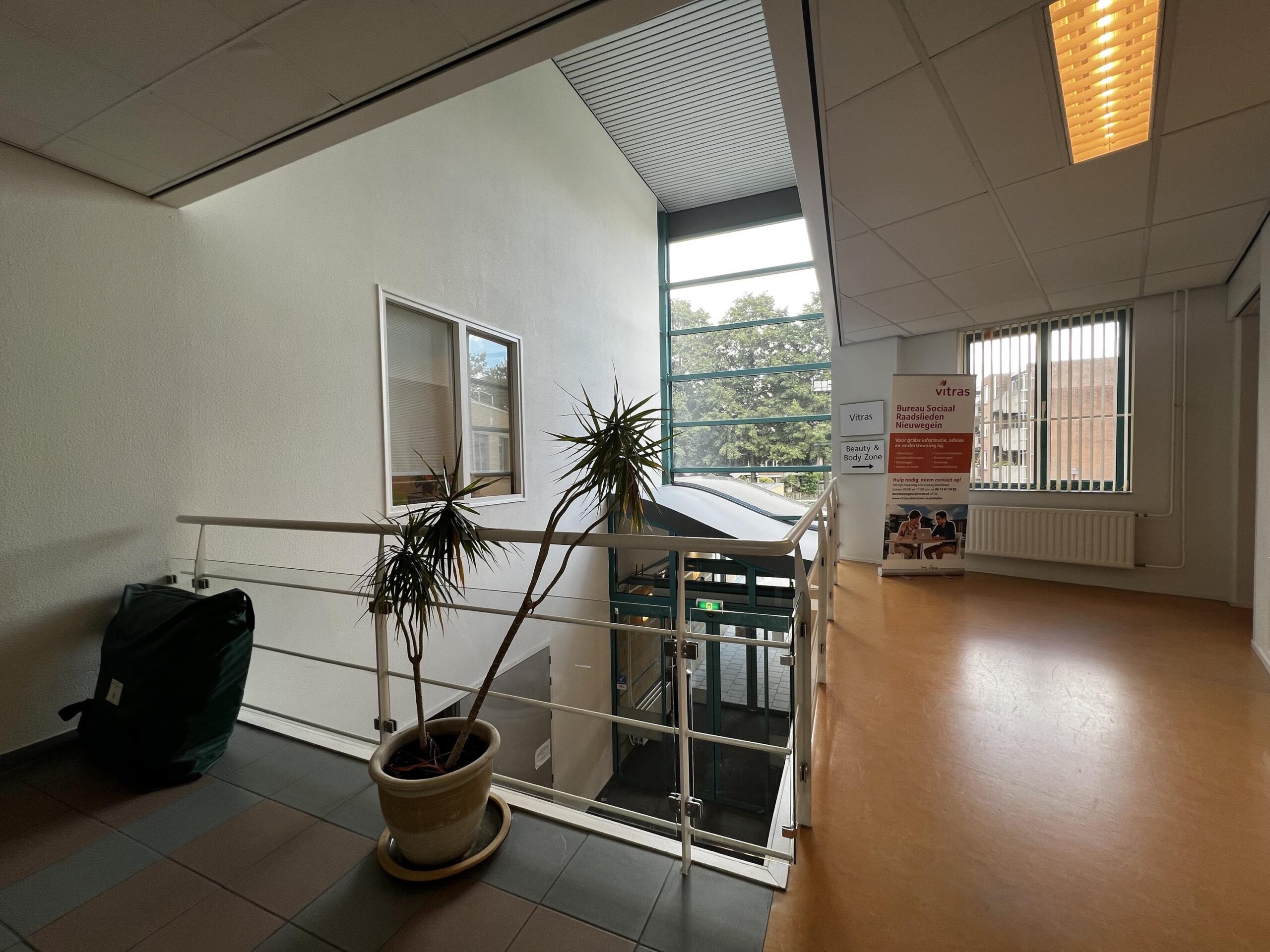 Een lichte overloop met een plant, zicht naar buiten en een bord van Bureau Sociaal Raadslieden Nieuwegein.