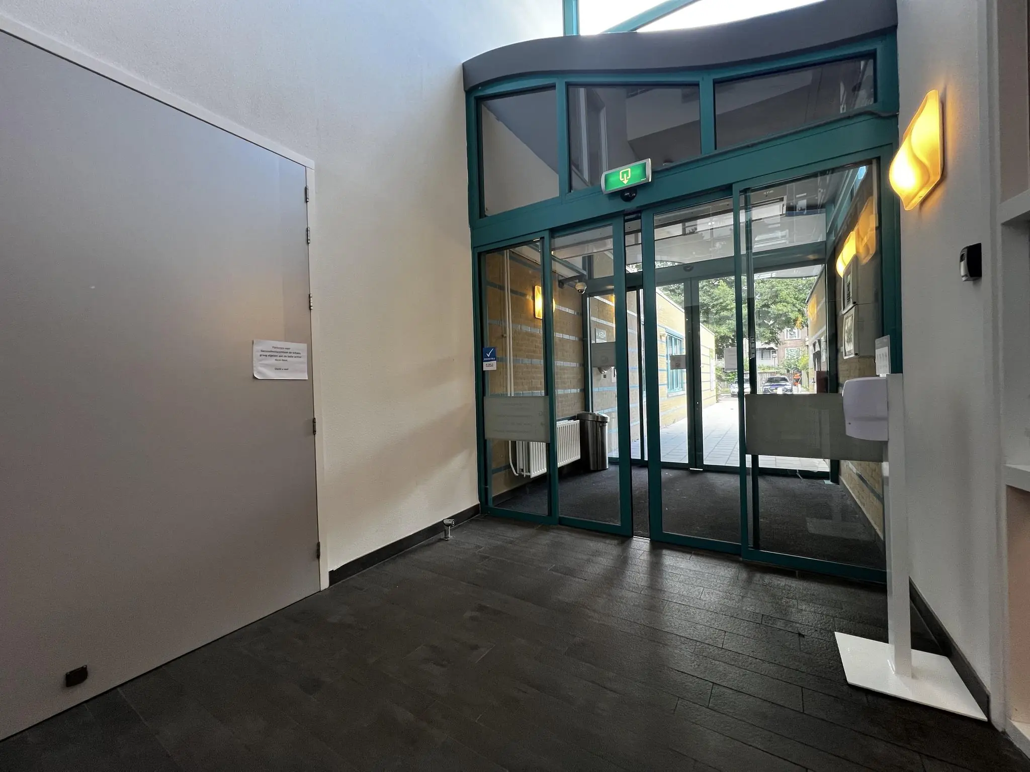 Ingang van het gebouw Zoutkamperschans met glazen schuifdeuren, een ontsmettingszuil en een bordje op een grijze deur.