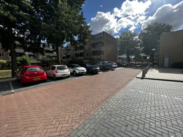 Parkeerplaats met geparkeerde auto's en appartementen aan de Zoutkamper Schans op een zonnige dag met deels bewolkte lucht.