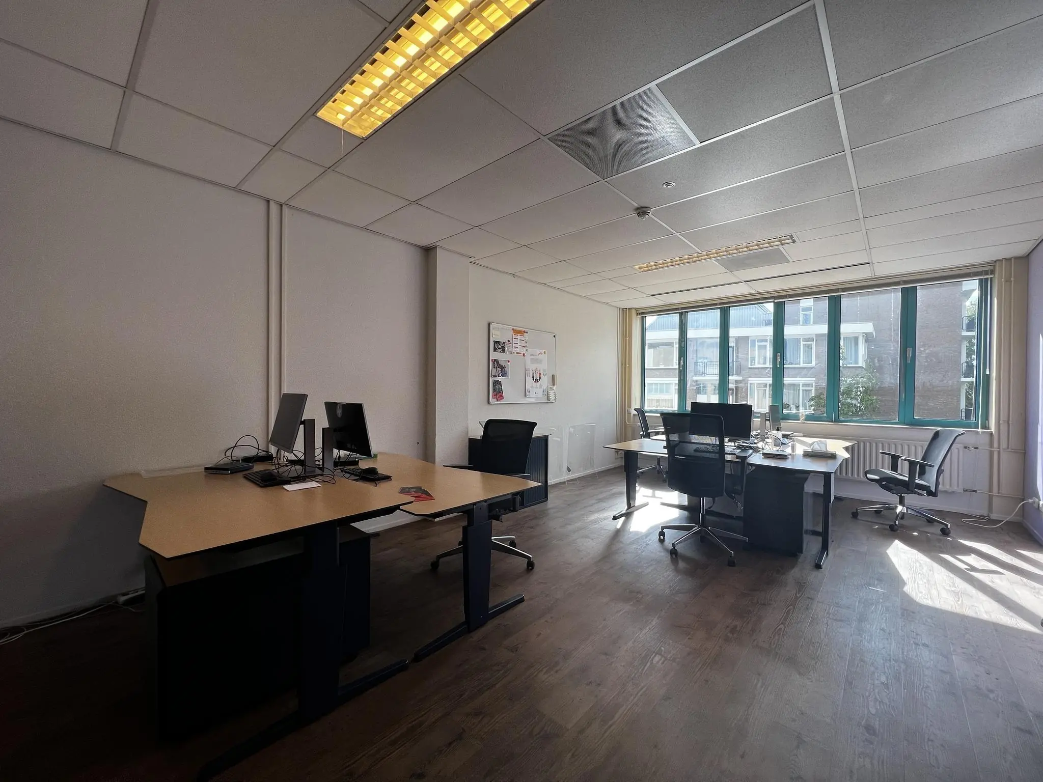 Kantoorruimte in Zoutkamper Schans met meerdere bureaus, computers en een groot raam dat uitzicht biedt op een wooncomplex.