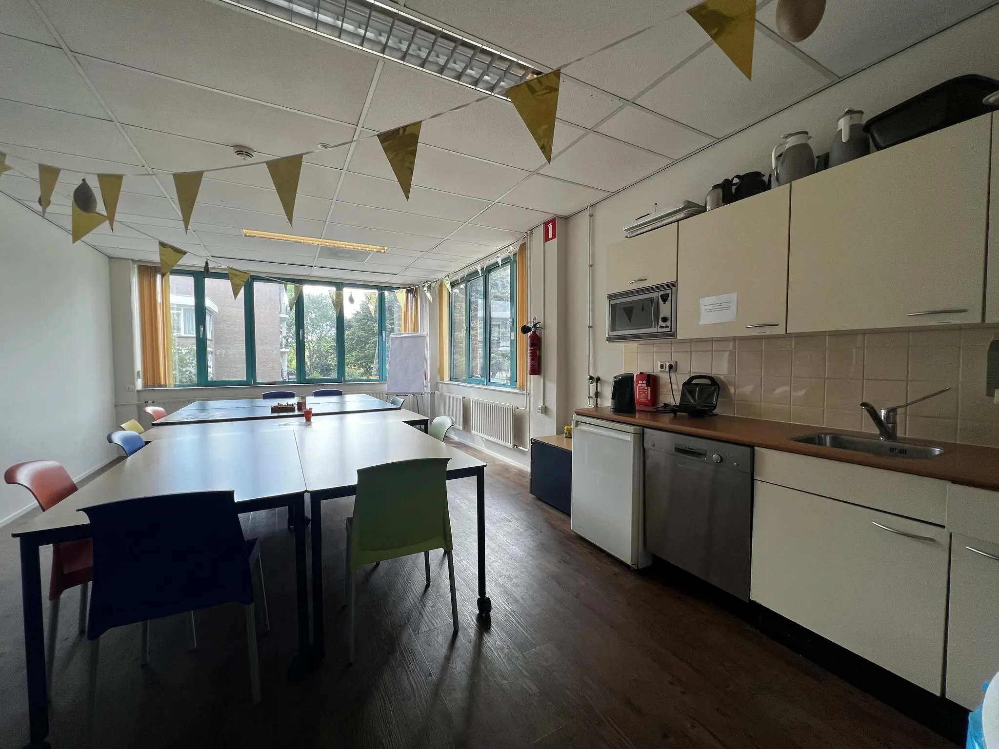 Gemeenschappelijke ruimte in Zoutkamperschans met keukentje, vergadertafels, kleurrijke stoelen en feestelijke vlaggetjes.