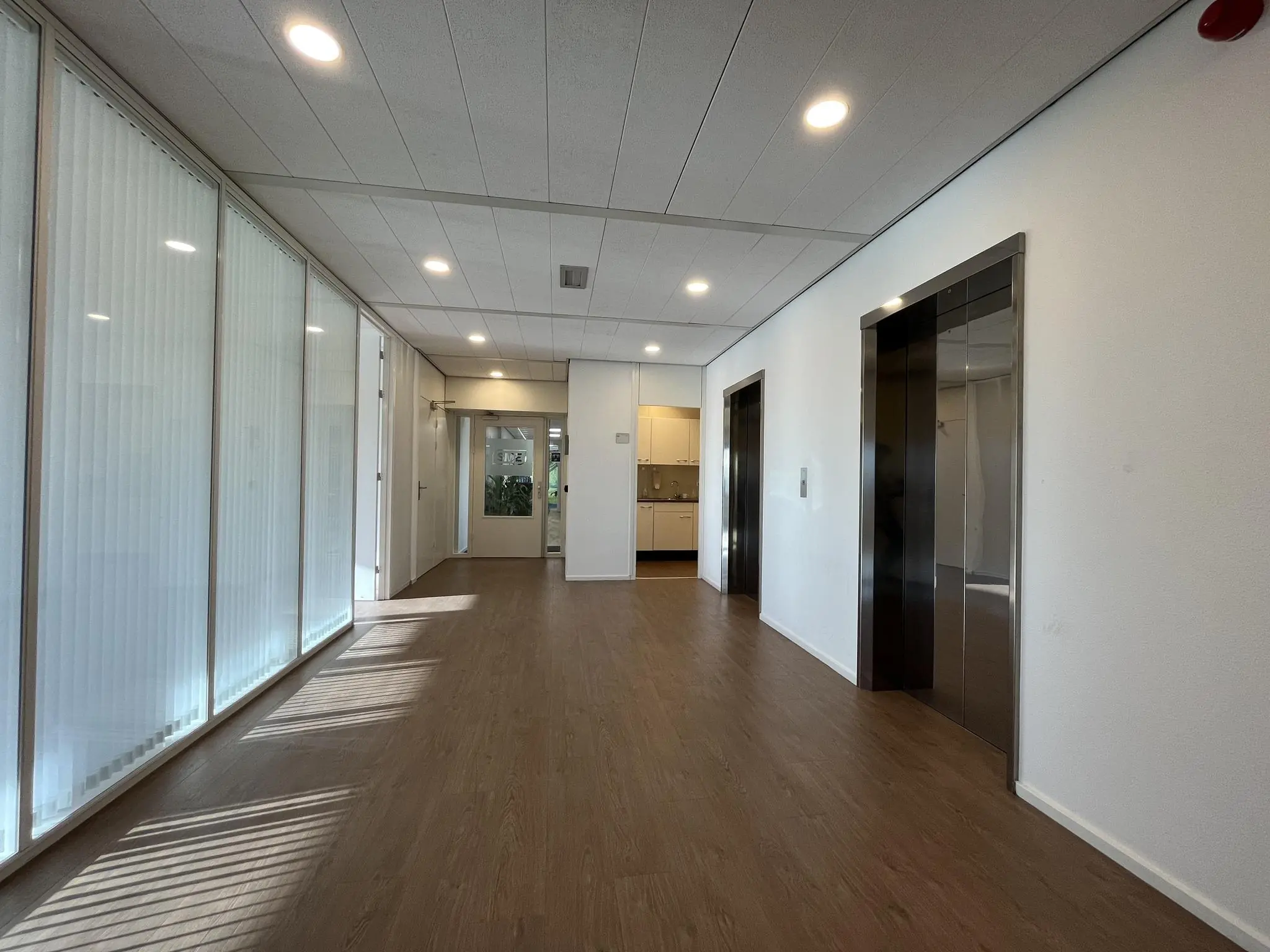 Moderne kantoorhal aan de Australiëlaan met houten vloer, glazen wanden en twee liften.