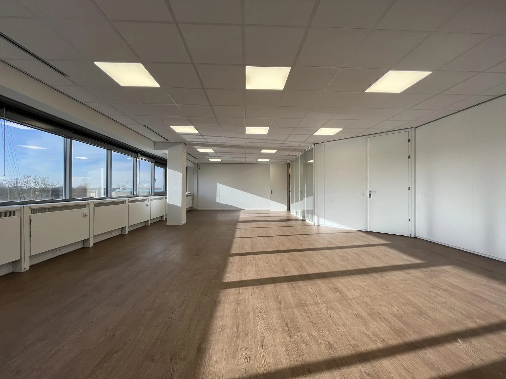 Lichte, lege kantoorruimte aan de Australiëlaan met houten vloer, systeemplafond en grote ramen.