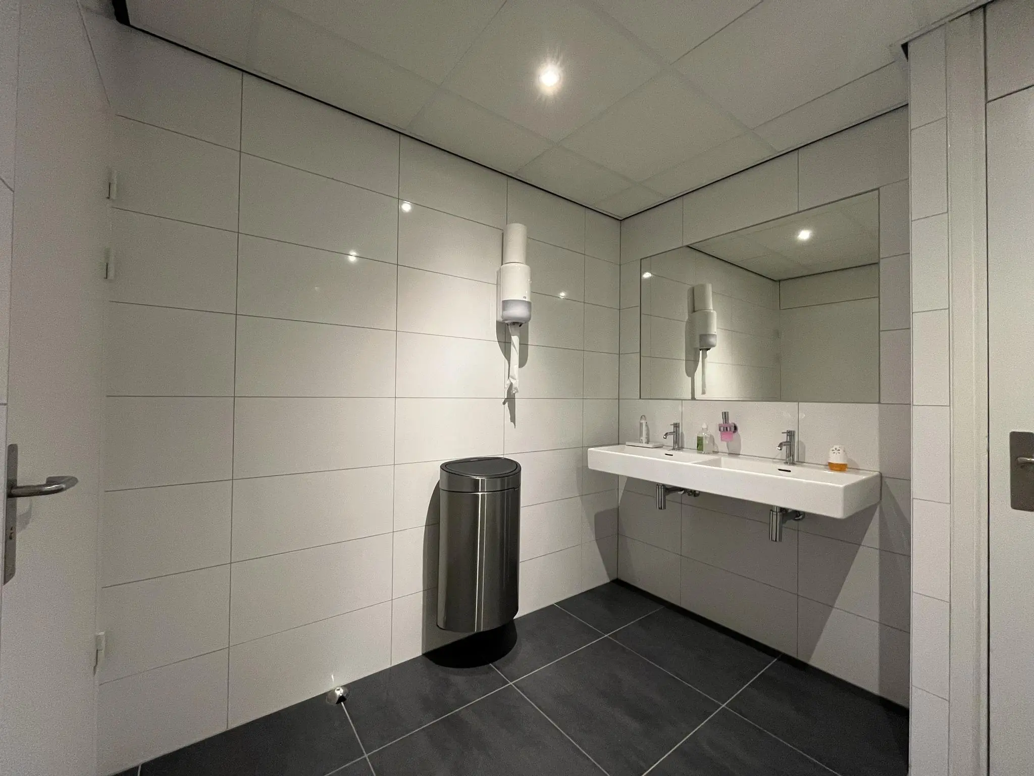 Moderne, betegelde wasruimte met dubbele wastafel, spiegel, afvalbak en zeepdispensers aan de Australielaan.