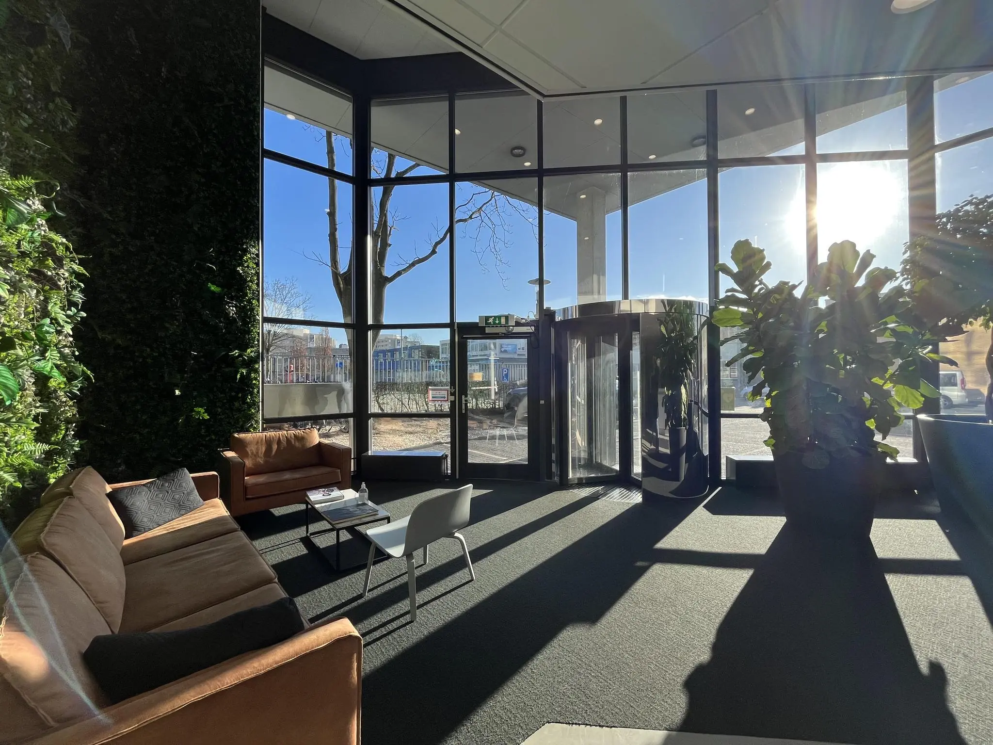 Moderne wachtruimte aan de Australielaan met grote ramen, zonlicht, planten en zithoek met banken.