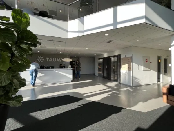 Inkomhal van het kantoorpand aan de Australielaan met een balie van TAUW, personen bij de receptie en liften in de achtergrond.