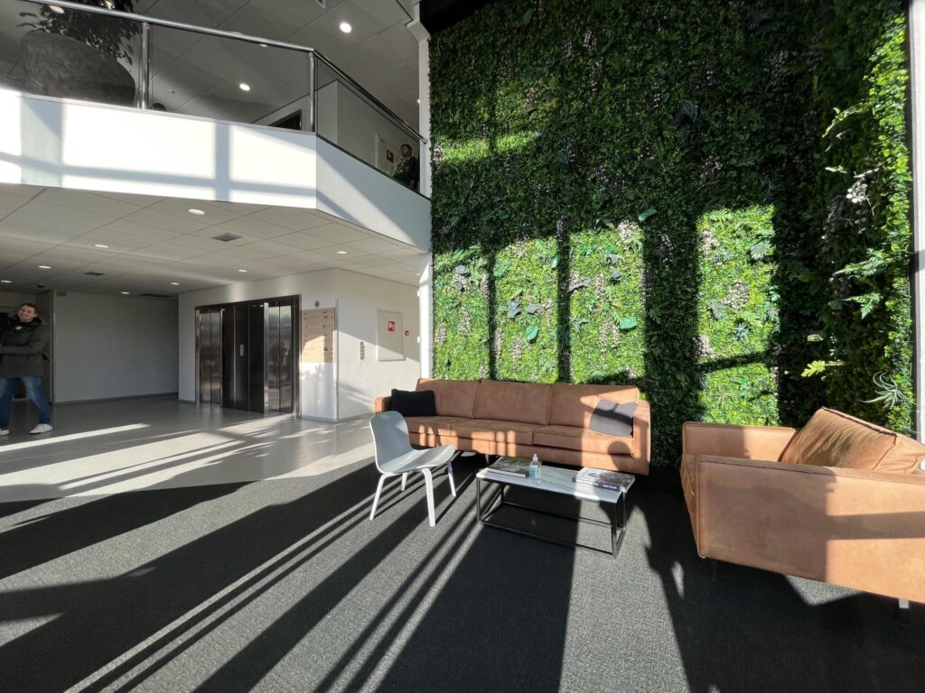 Moderne ontvangsthal aan de Australielaan met een groene plantenwand, zitbanken en veel natuurlijk licht.