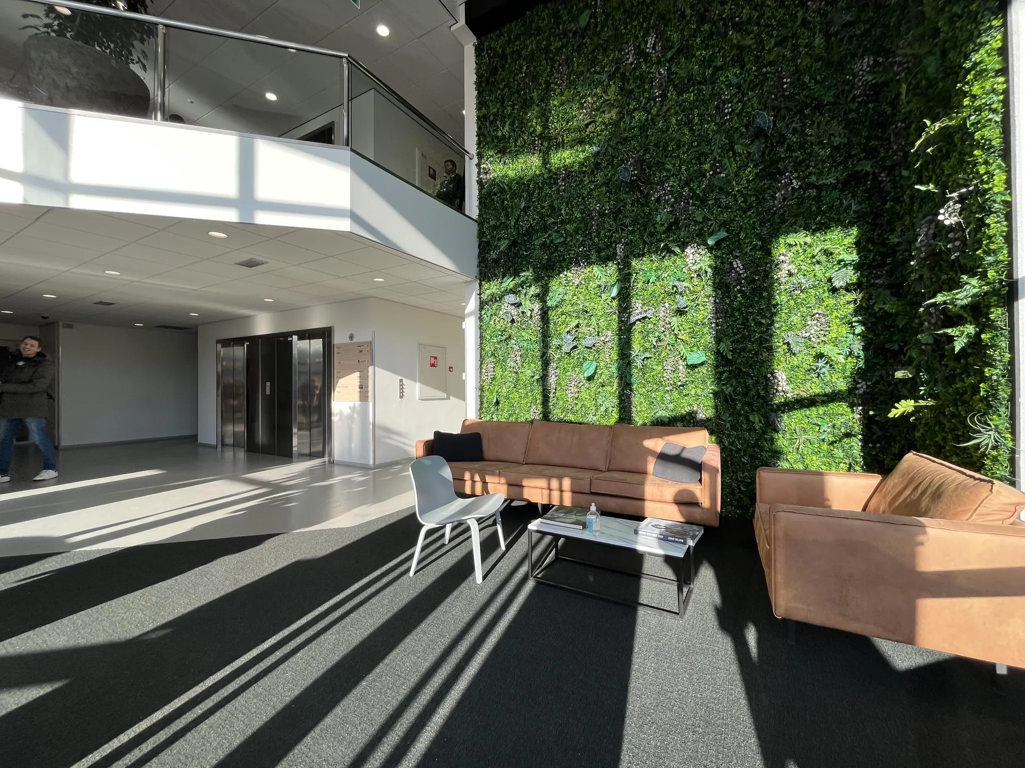 Moderne ontvangsthal aan de Australielaan met een groene plantenwand, zitbanken en veel natuurlijk licht.