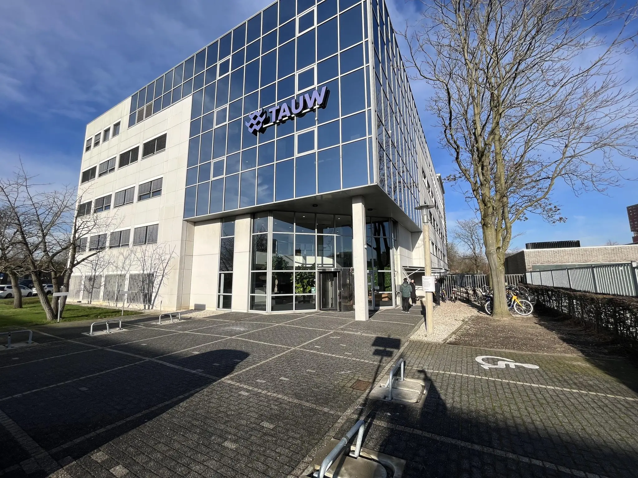 Kantoorgebouw van TAUW aan de Australielaan met glazen gevel en fietsenstalling bij de ingang.