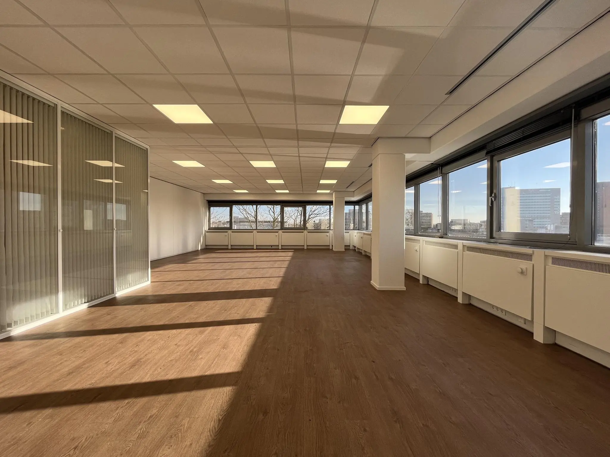 Lichte, lege kantoorruimte aan de Australiëlaan met houten vloer, systeemplafond en grote ramen met uitzicht op de stad.