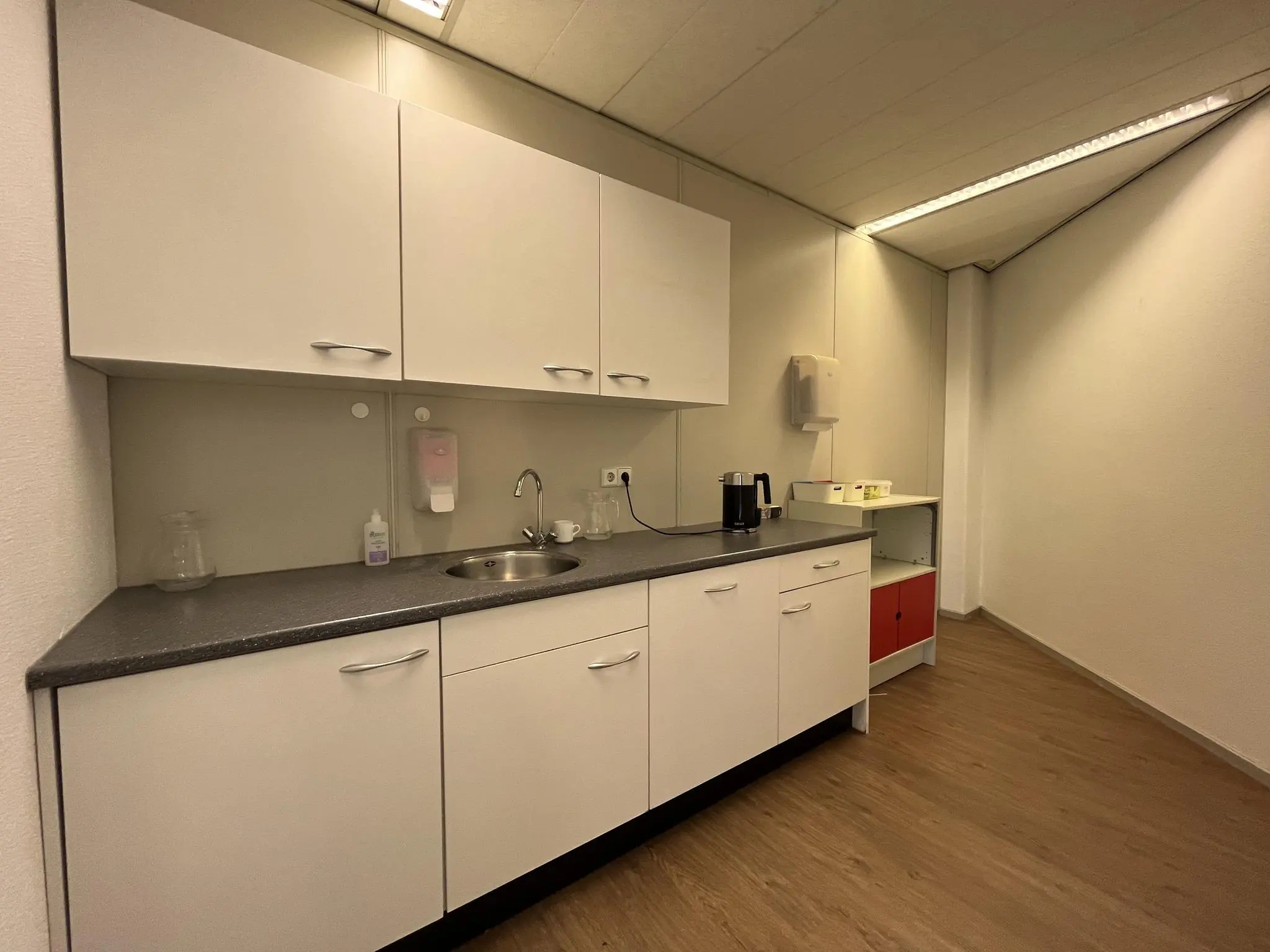 Keukenblok in een kantoorruimte aan de Australiëlaan met witte kasten, gootsteen en koffiezetapparaat.