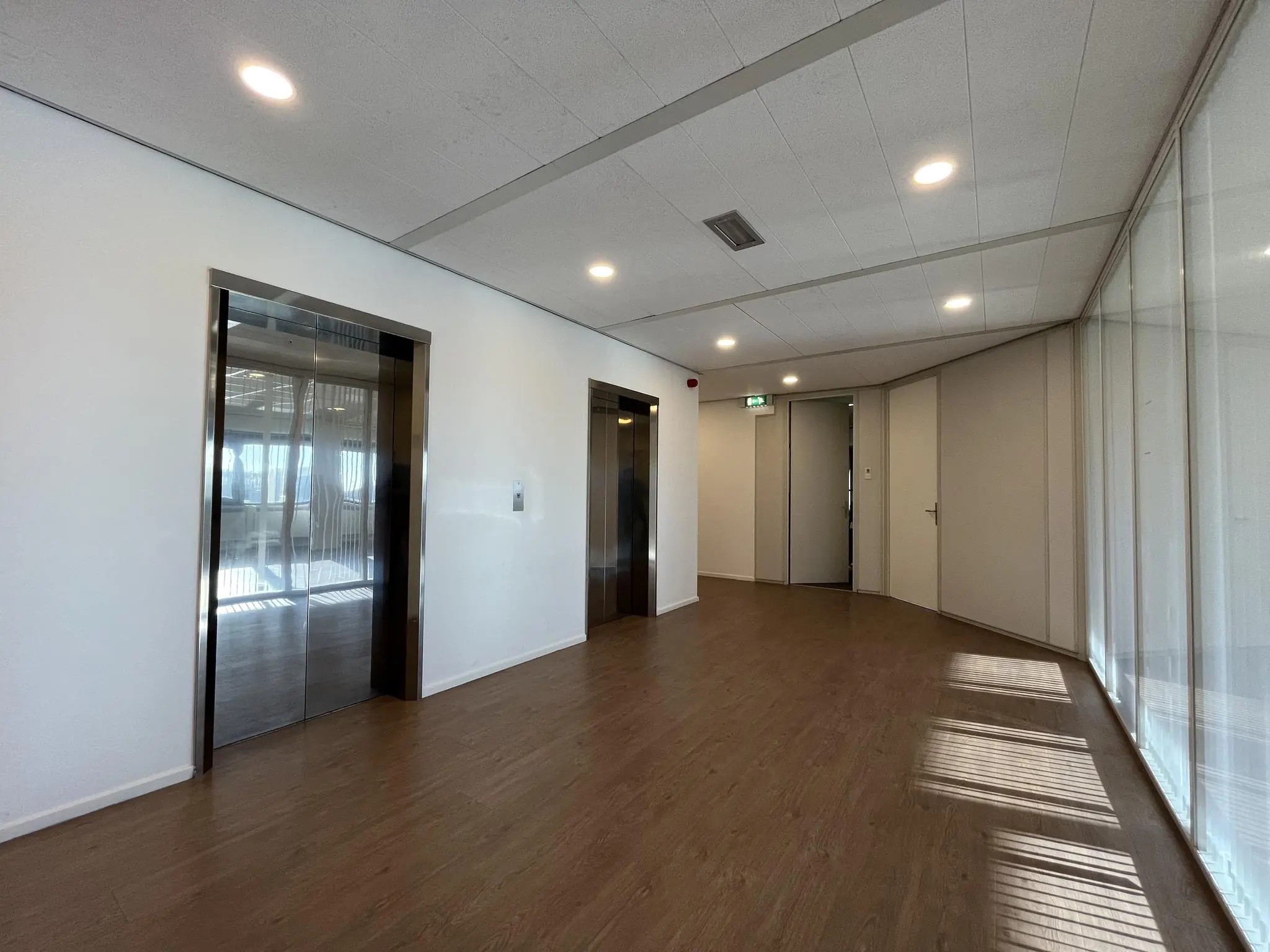 Moderne kantoorhal aan de Australiëlaan met twee liften, houten vloer en glazen wand.