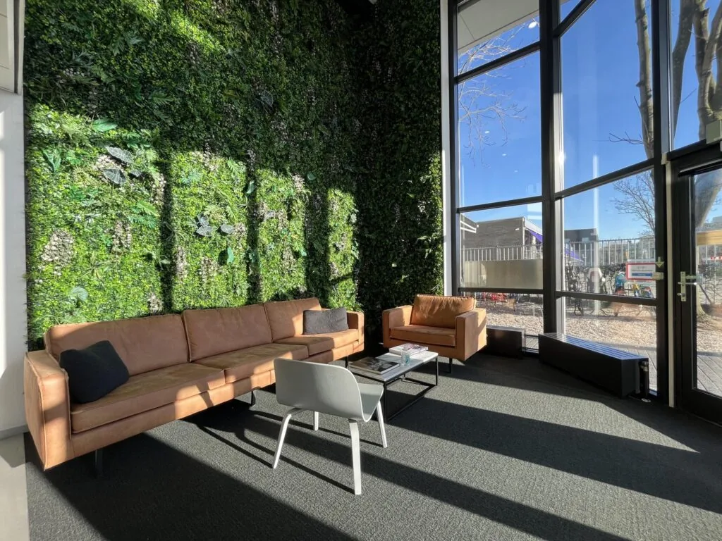 Moderne wachtruimte aan de Australiëlaan met een groene plantenmuur, leren zitbanken en grote ramen die veel daglicht binnenlaten.