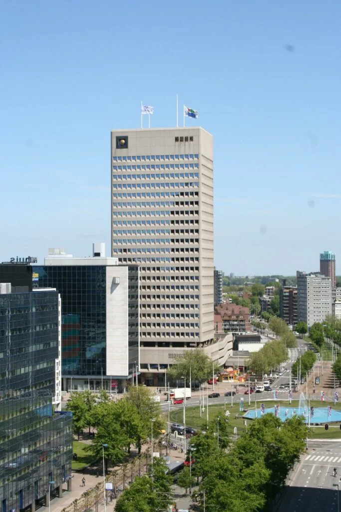 Hoog kantoorgebouw aan het Hofplein in Rotterdam met fontein en druk stadsverkeer op de voorgrond.