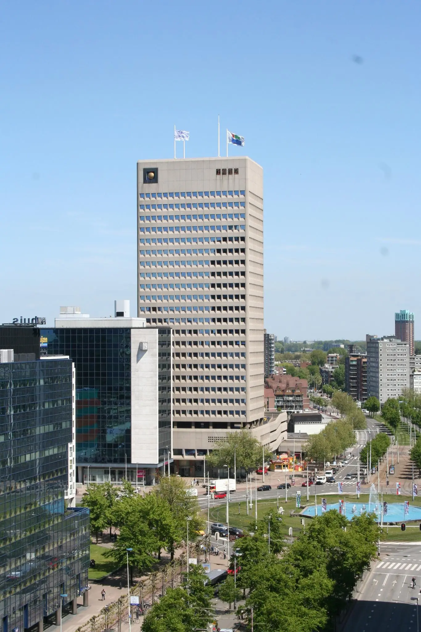 Hoog kantoorgebouw aan het Hofplein in Rotterdam met fontein en druk stadsverkeer op de voorgrond.