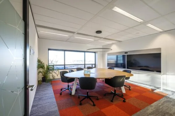 Moderne vergaderruimte op Radarweg met ovale tafel, zes stoelen, groot videoscherm en panoramisch raam.