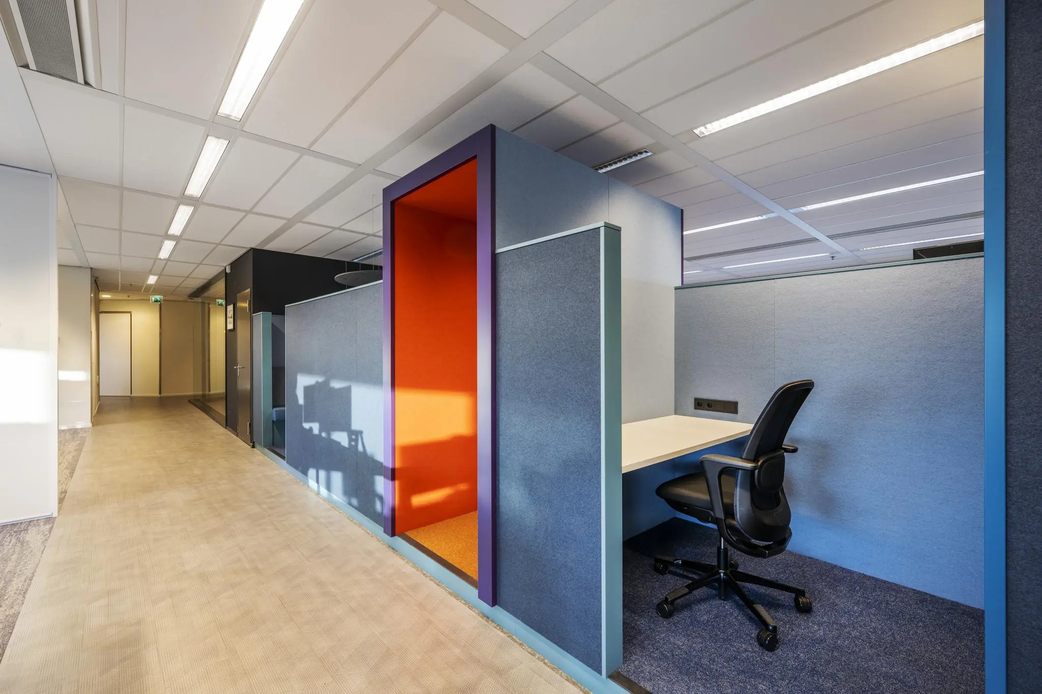 Moderne kantoorgang met open werkplekken en feloranje akoestische belcel aan de Radarweg.