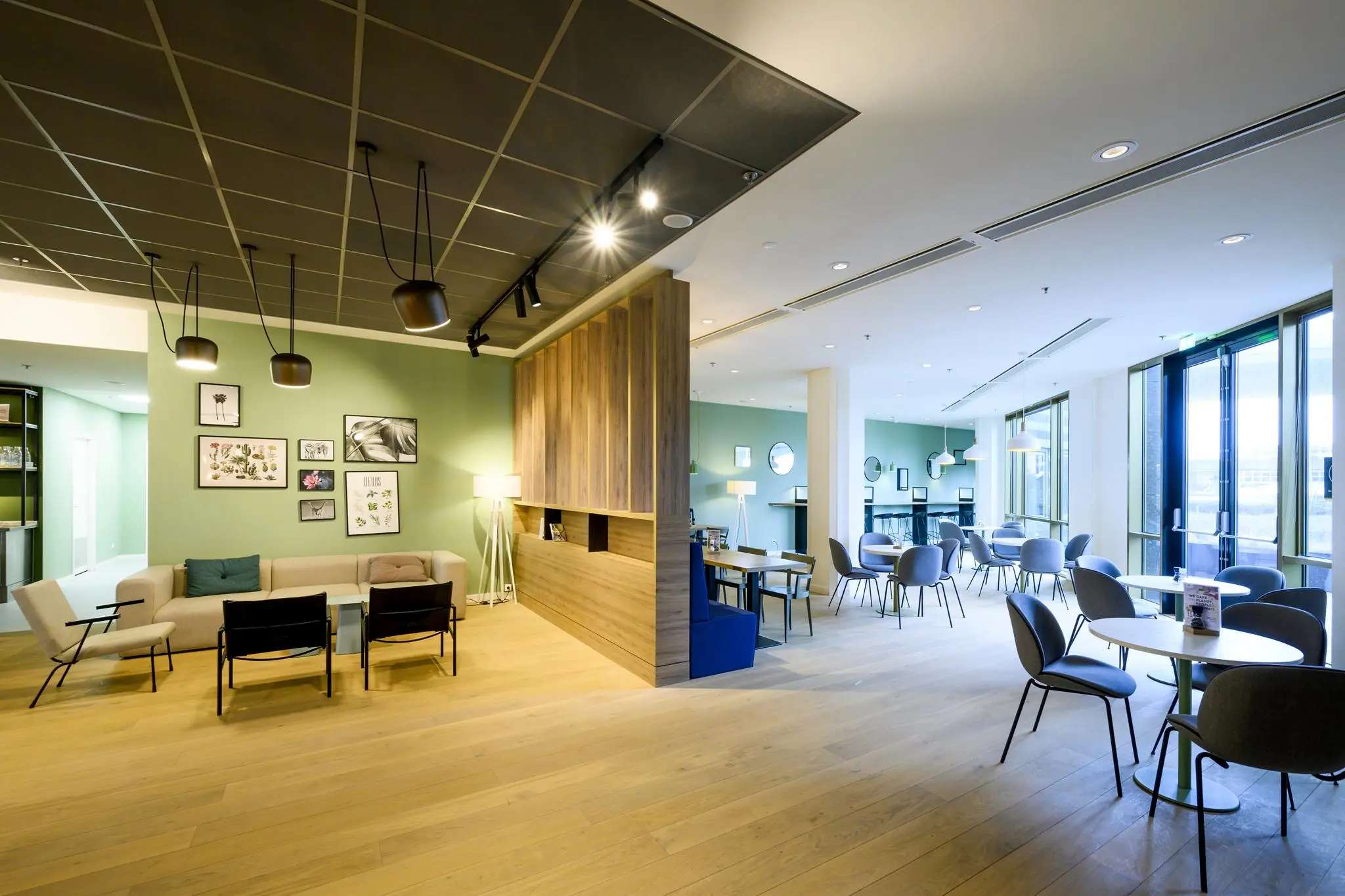 Modern ingerichte loungeruimte aan de Radarweg met zitgedeelte, eettafels en grote ramen die veel daglicht binnenlaten.