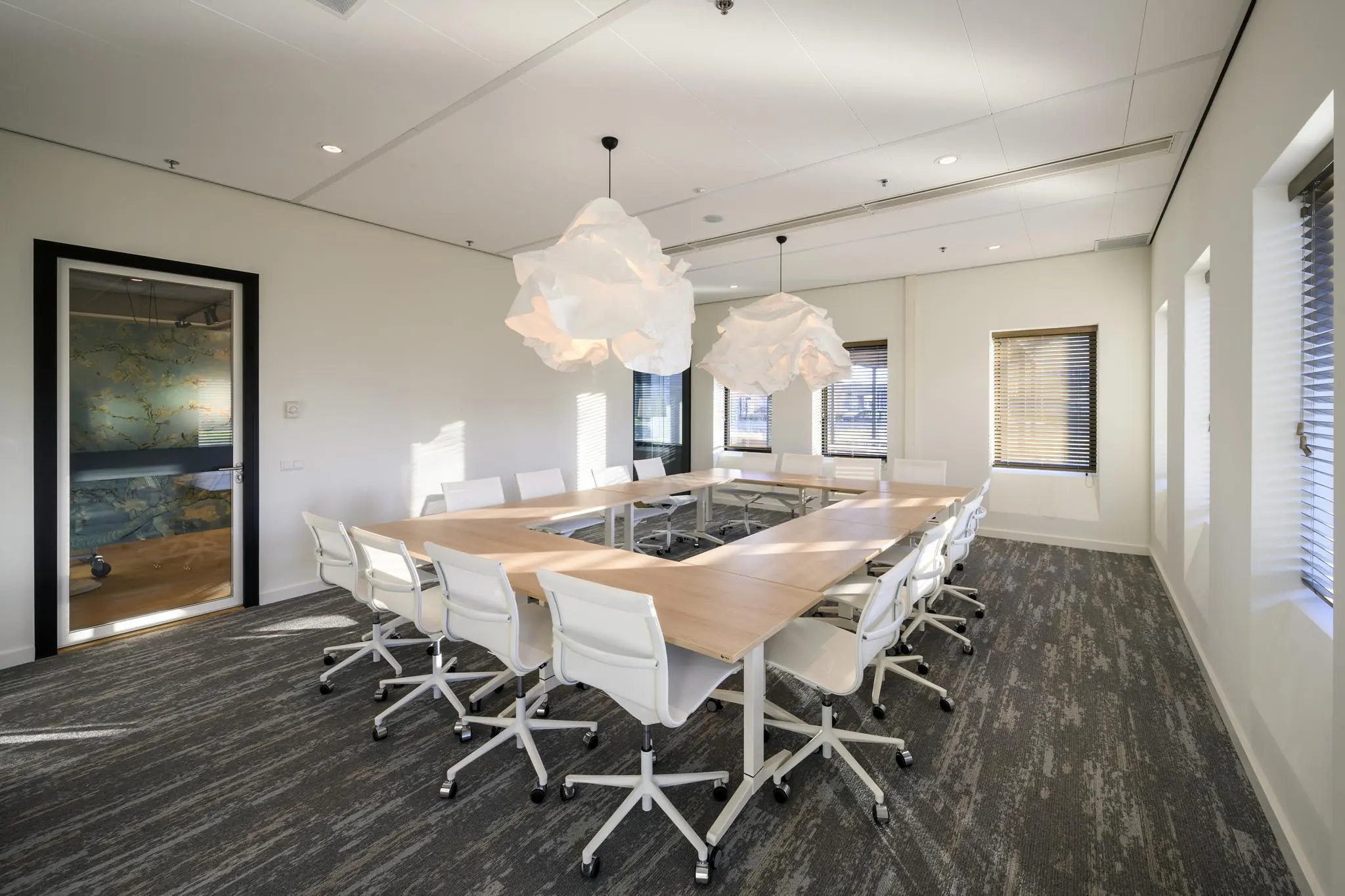 Vergaderruimte met U-vormige tafelopstelling, witte stoelen en opvallende hanglampen aan de Radarweg.