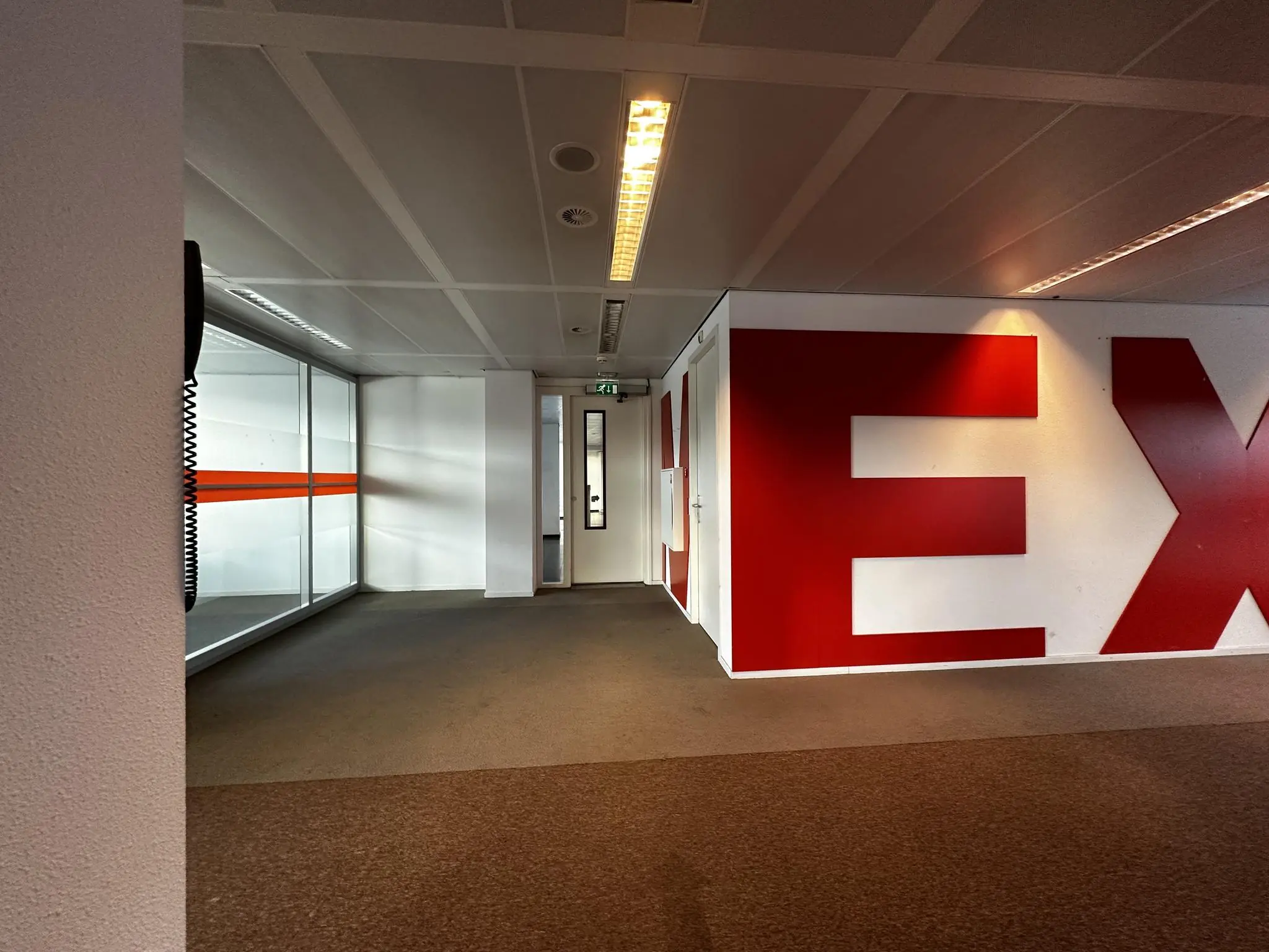 Leeg kantoorpand aan de Europalaan met witte wanden, rood opschrift en glazen wand met oranje streep.