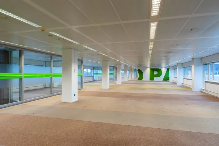 Leeg kantoorpand aan de Europalaan met tapijtvloer, systeemplafond en glazen wanden met groene accenten.